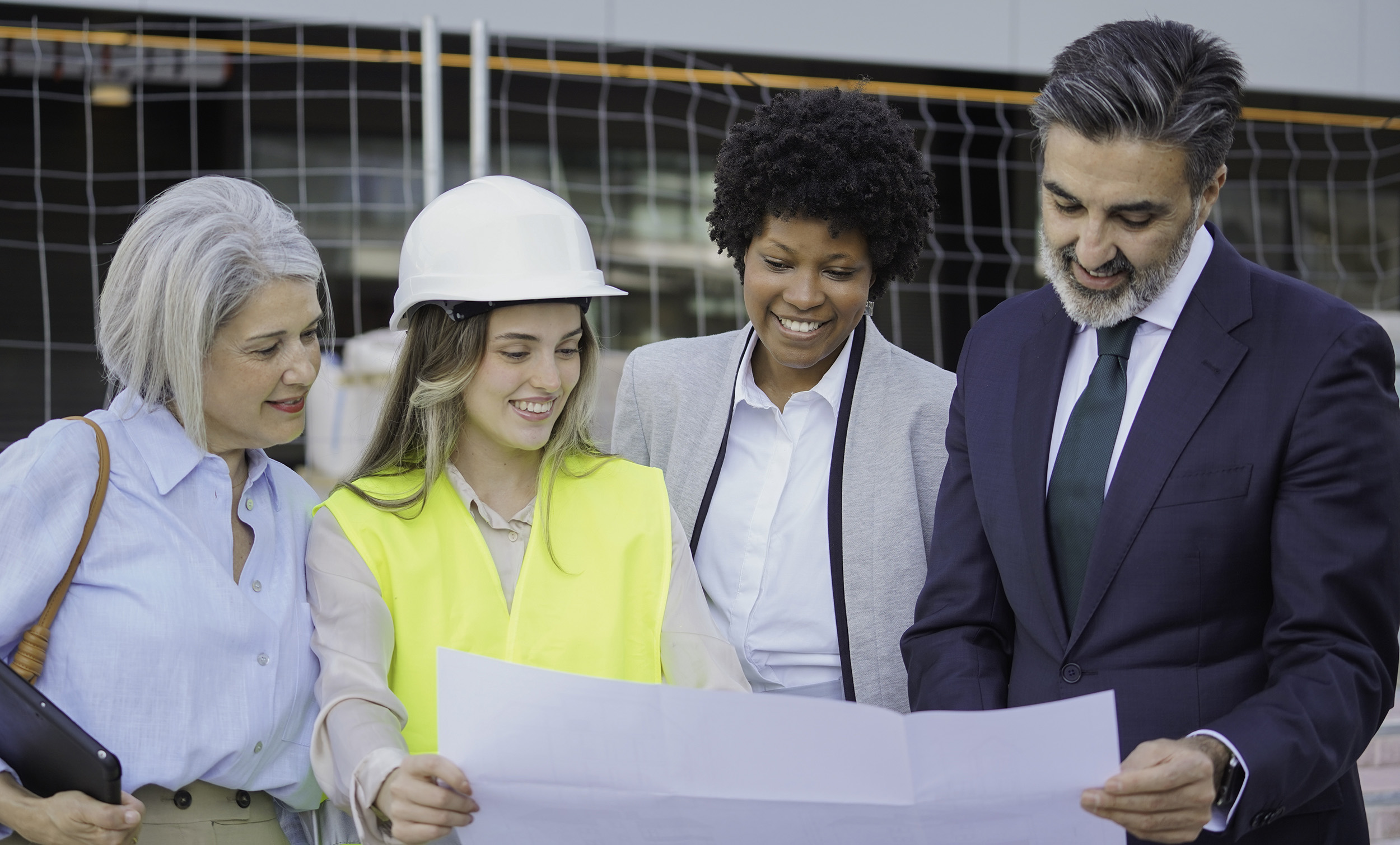 Smiling architects and engineers examining blueprint on construction site Project Managers & Construction Executives